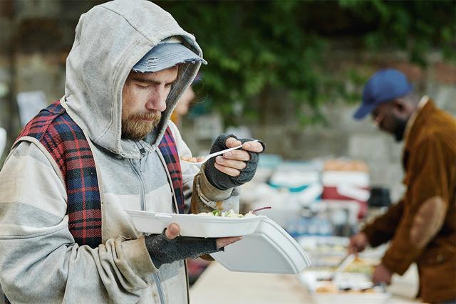 Homeless man eats from street van.